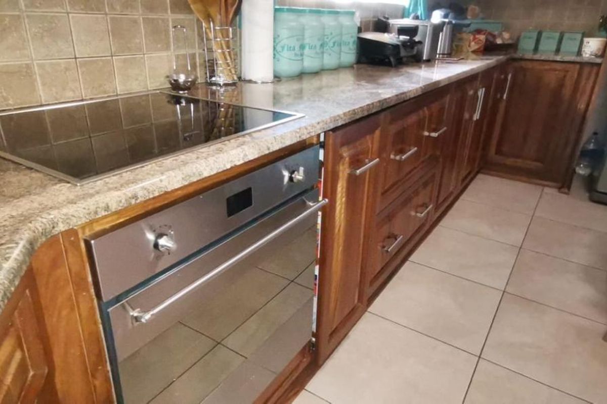 A functional kitchen featuring dark wood cabinetry, granite countertops, a built-in oven, and a glass cooktop with tiled backsplash.