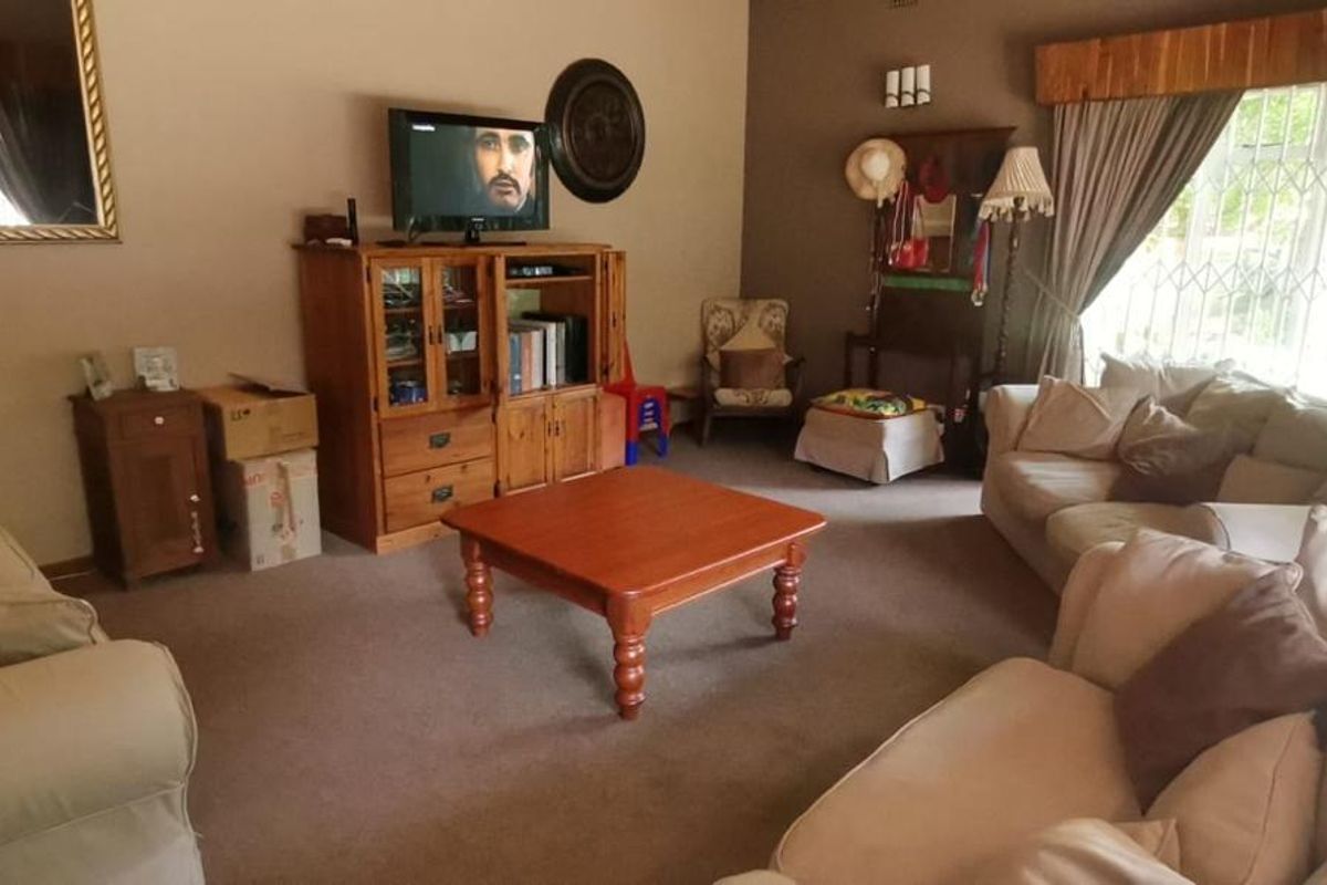 A spacious living room featuring neutral carpeting, large windows with security bars, and a classic layout suitable for comfortable family living.
