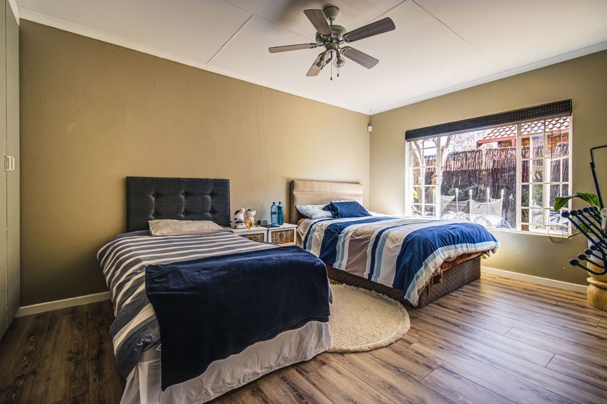 Spacious bedroom featuring wood-look laminate flooring, a ceiling fan, and large windows providing natural light and garden views.
