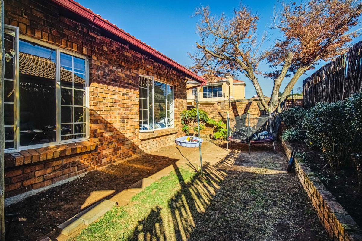 A rear garden area featuring a face-brick exterior wall, large windows, and a landscaped yard with a retaining wall and mature trees.