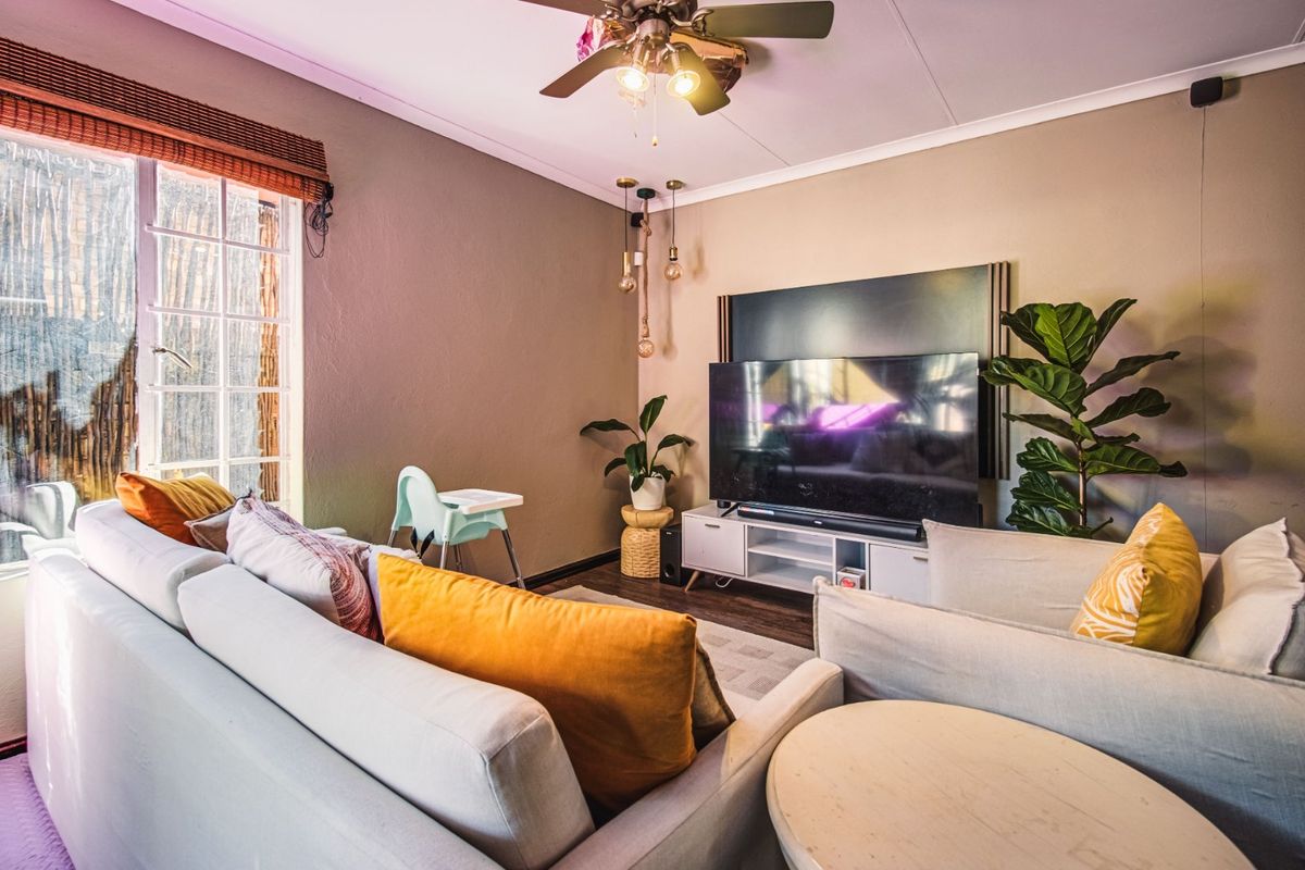 A cozy living room featuring a ceiling fan, neutral wall tones, and large windows that provide natural light to the space.