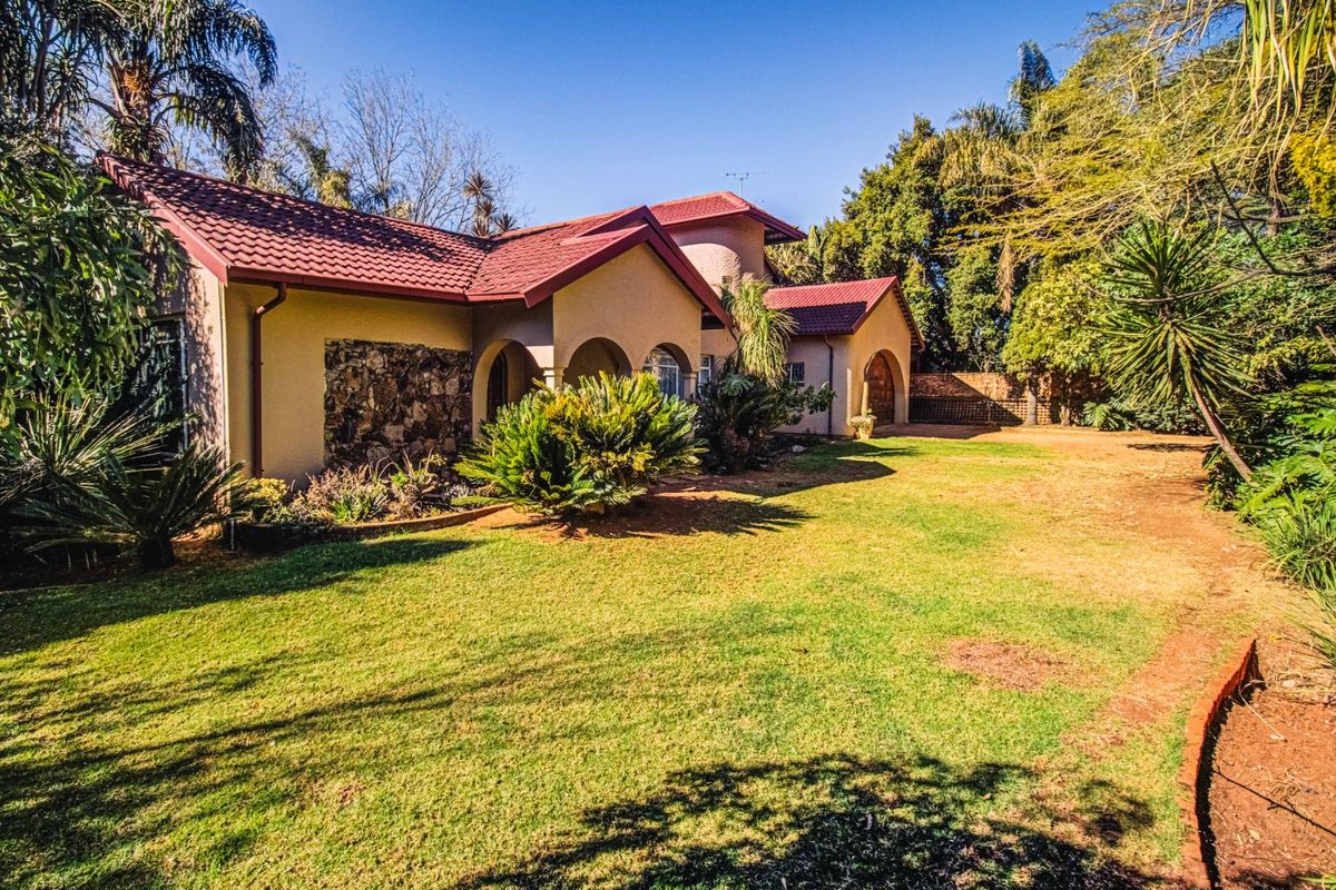 A view of the rear exterior of the house, featuring a tiled roof, arched covered patio, stone cladding detail, and a spacious lawn.