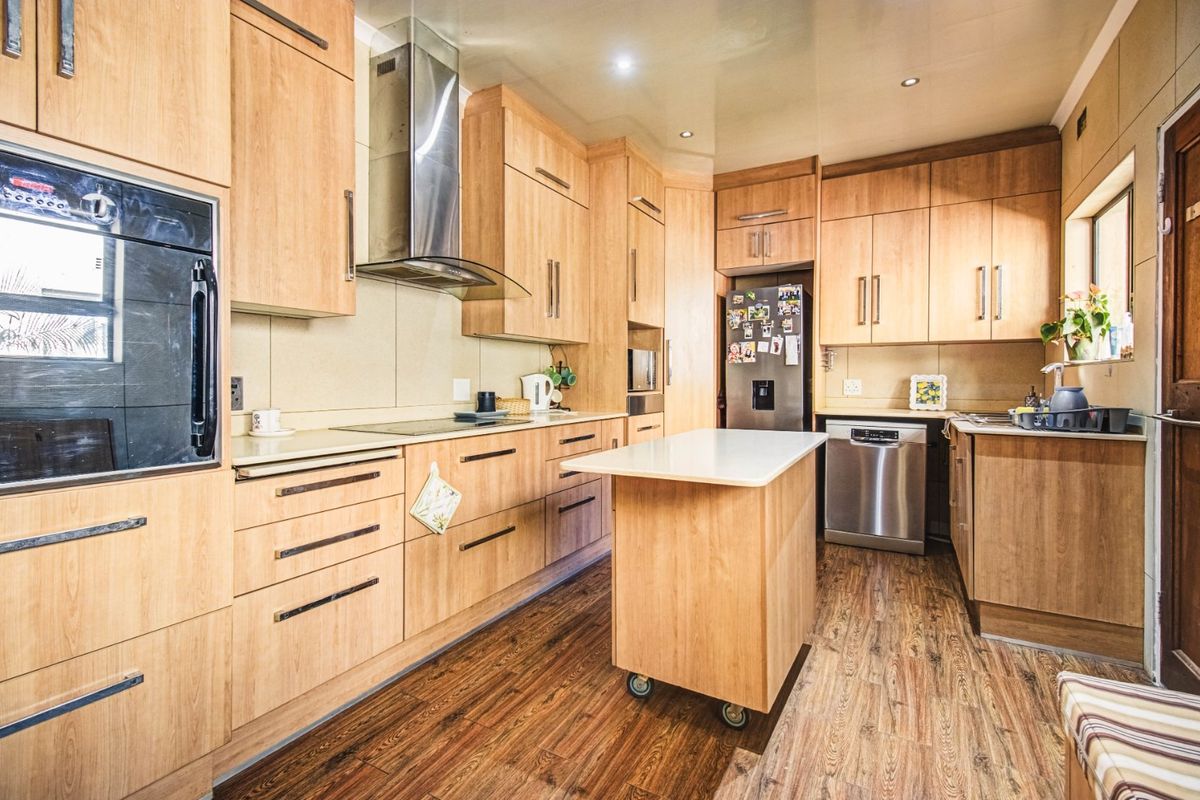 A functional kitchen featuring light wood cabinetry, a central mobile island, stainless steel extractor fan, built-in oven, and wood-look flooring.