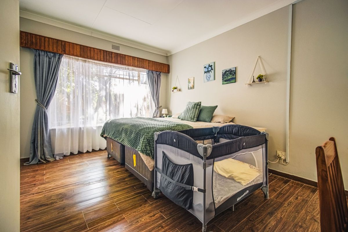 A bedroom featuring wood-look flooring, a large window with a wooden pelmet, and neutral wall finishes.