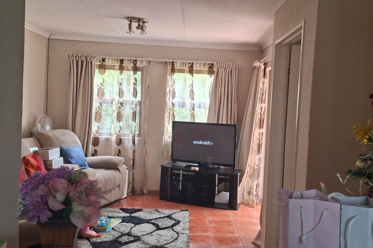 A view into a living room featuring tiled flooring and dual windows with curtains, providing a functional and comfortable living space.
