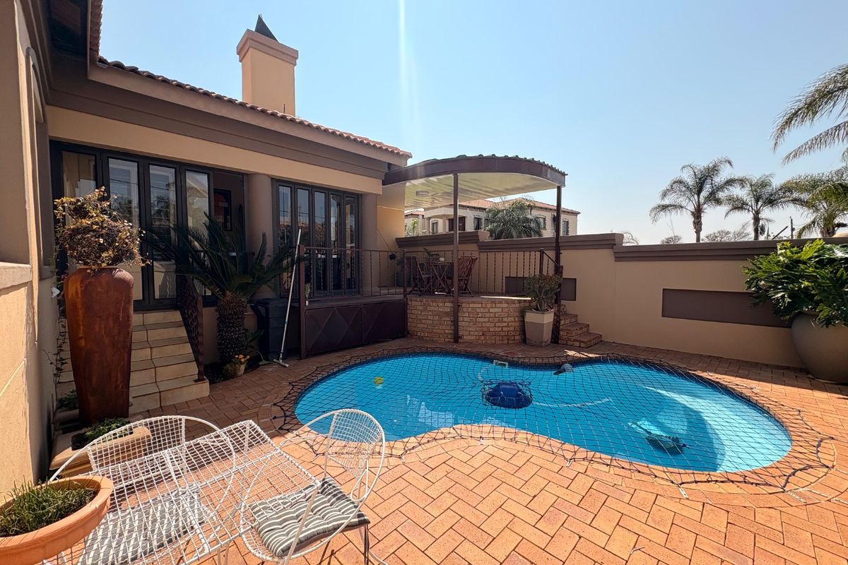A private outdoor pool area featuring paved surrounds, a built-in brick braai area, and direct access to the home via folding glass doors.