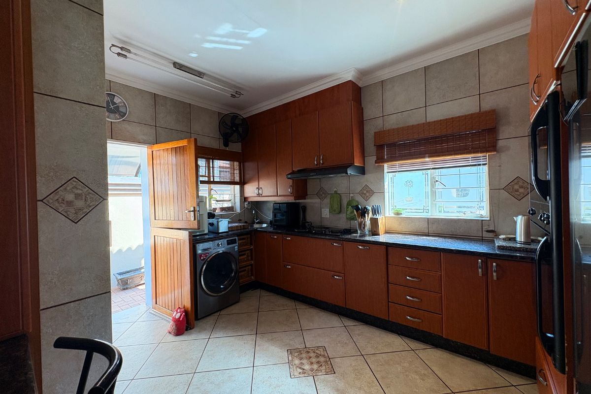 Functional kitchen featuring wood-toned cabinetry, granite countertops, tiled flooring, and integrated laundry space with direct access to the exterior.