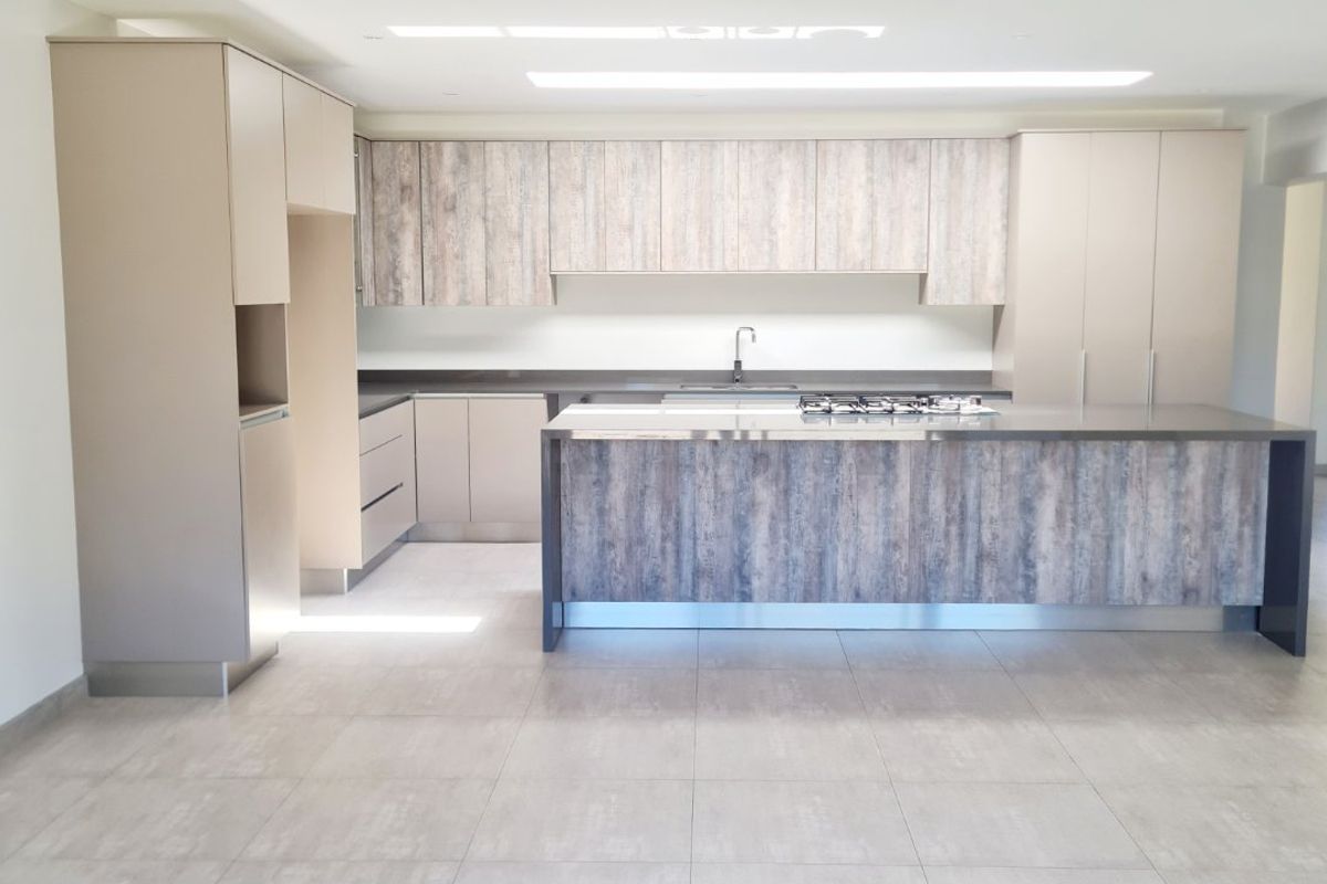 Modern open-plan kitchen featuring a large central island with integrated gas hob, sleek cabinetry, and neutral floor tiling.