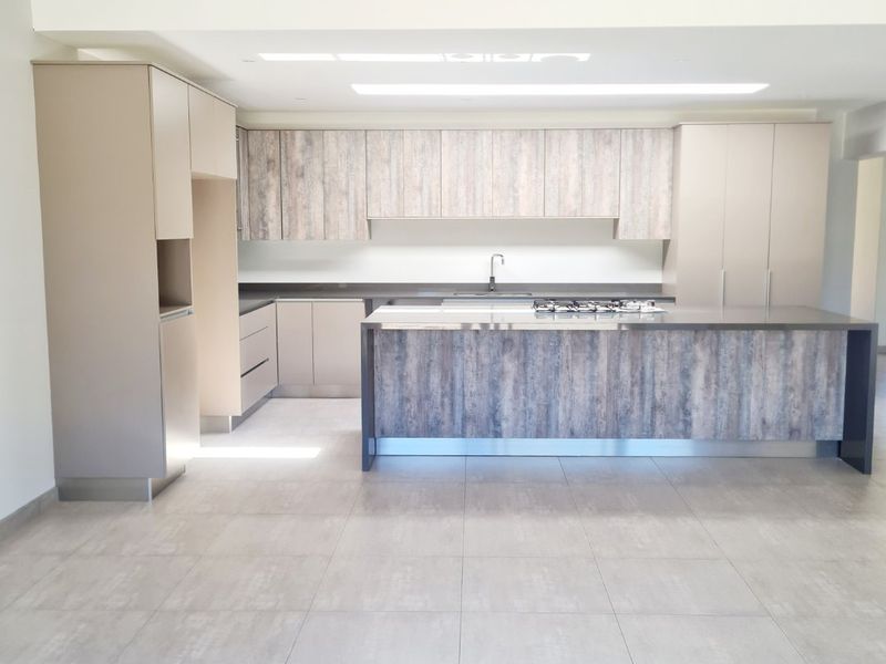 Modern open-plan kitchen featuring a large central island with integrated gas hob, sleek cabinetry, and neutral floor tiling.
