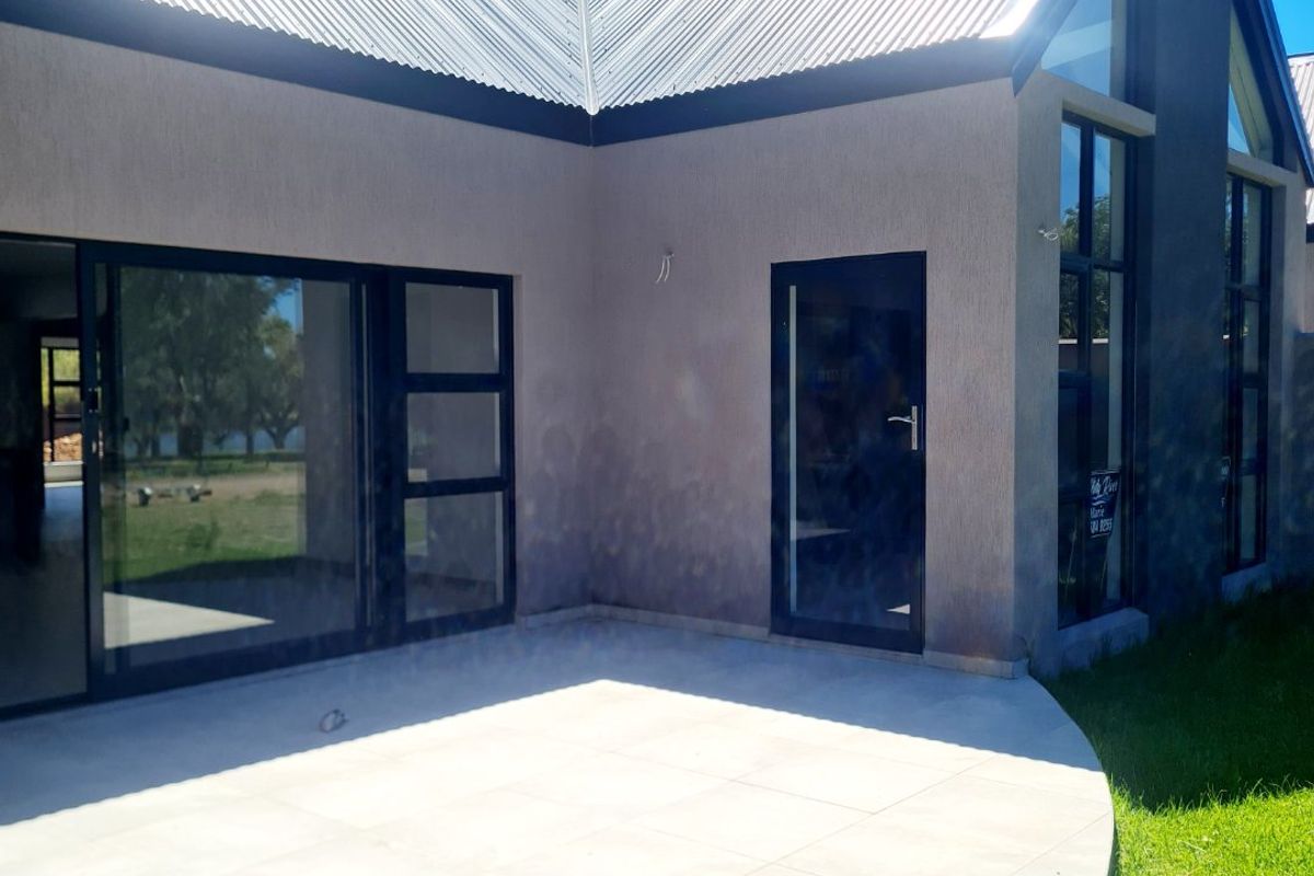 Modern rear exterior view featuring a tiled patio, large glass sliding doors, and high-pitched corrugated metal roofing.