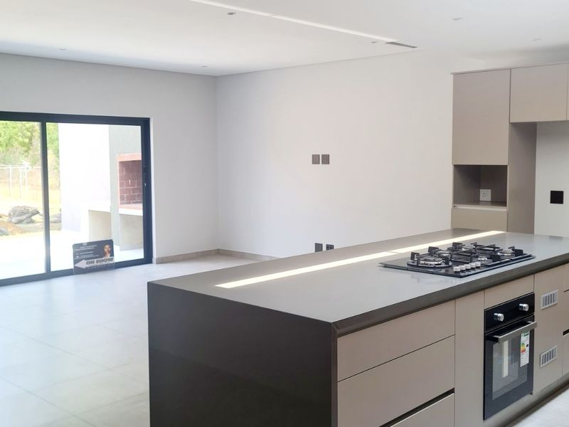 Modern open-plan kitchen featuring a large central island with integrated gas hob and oven, sleek cabinetry, and large format floor tiles.