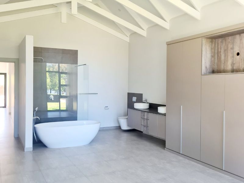 Spacious modern bathroom featuring a vaulted ceiling with exposed beams, a freestanding bathtub, dual vanity, and large format floor tiles.