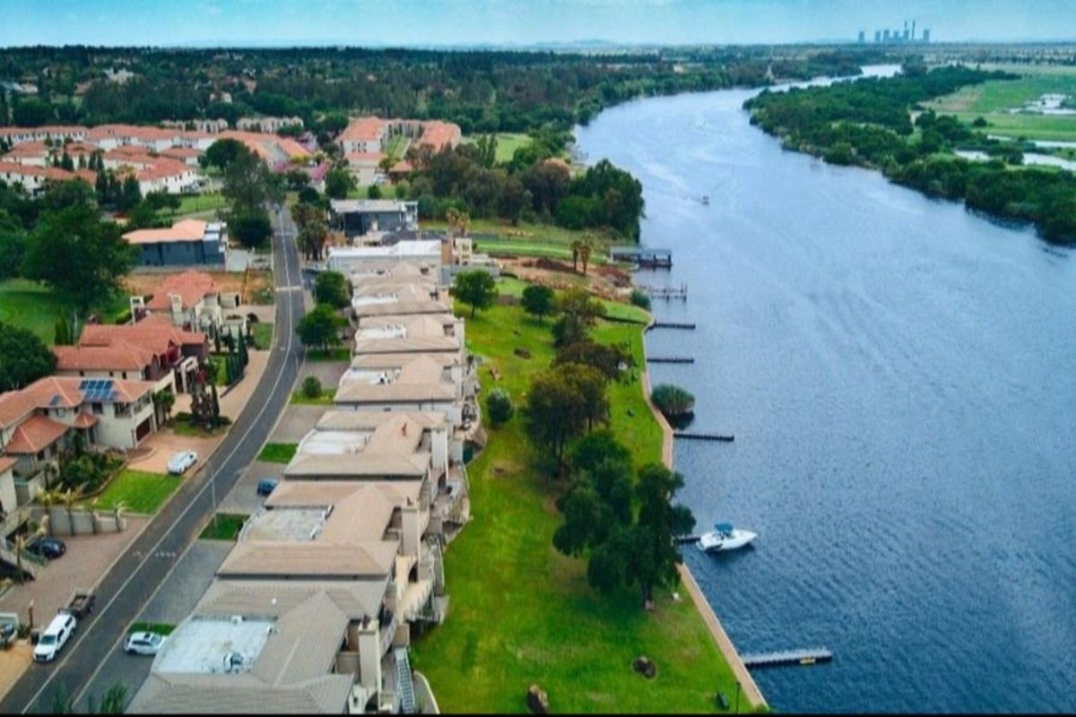 Aerial view of a residential estate situated along a riverbank, featuring landscaped green spaces, private jetties, and established suburban housing.