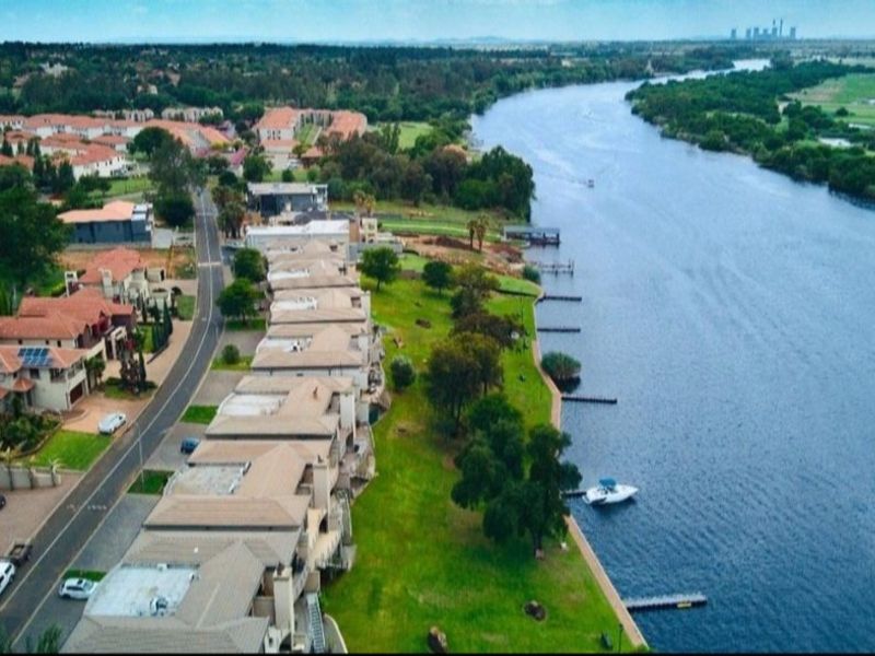 Aerial view of a residential estate situated along a riverbank, featuring landscaped green spaces, private jetties, and established suburban housing.
