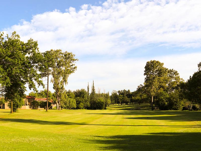 A scenic view of a well-maintained grassy landscape and mature trees, characteristic of a residential estate or golf course setting.