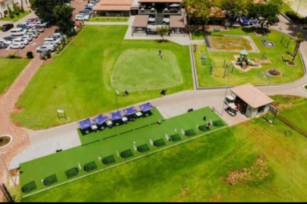 Aerial view of a well-maintained golf driving range facility featuring manicured greens, paved pathways, and associated clubhouse infrastructure within a residential estate.