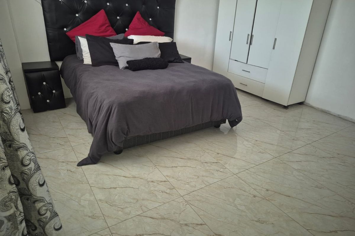 A bedroom featuring large-format marble-look floor tiles and a built-in wardrobe, offering a clean and functional living space.
