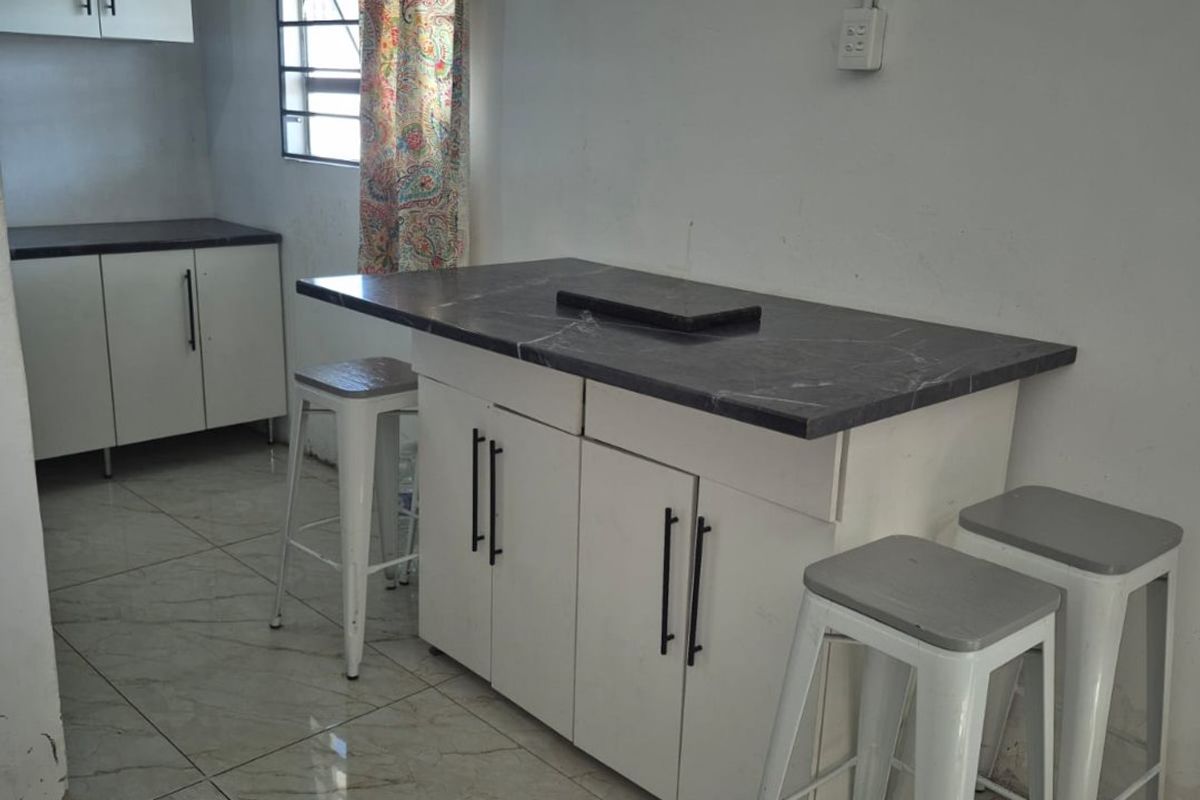 A functional kitchen area featuring white cabinetry, dark stone-look countertops, and light-colored floor tiles with a window providing natural light.