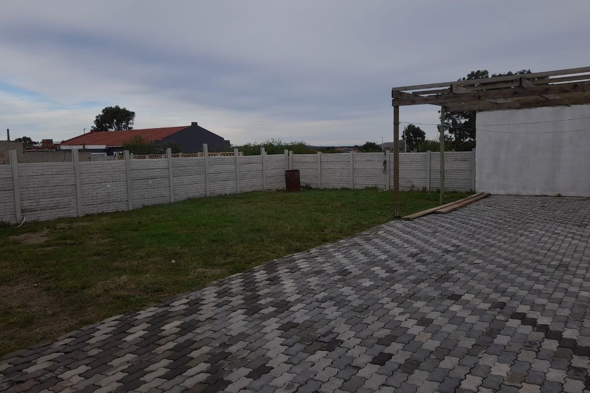 A spacious rear garden featuring a paved patio area, a timber pergola structure, and perimeter precast concrete walling.