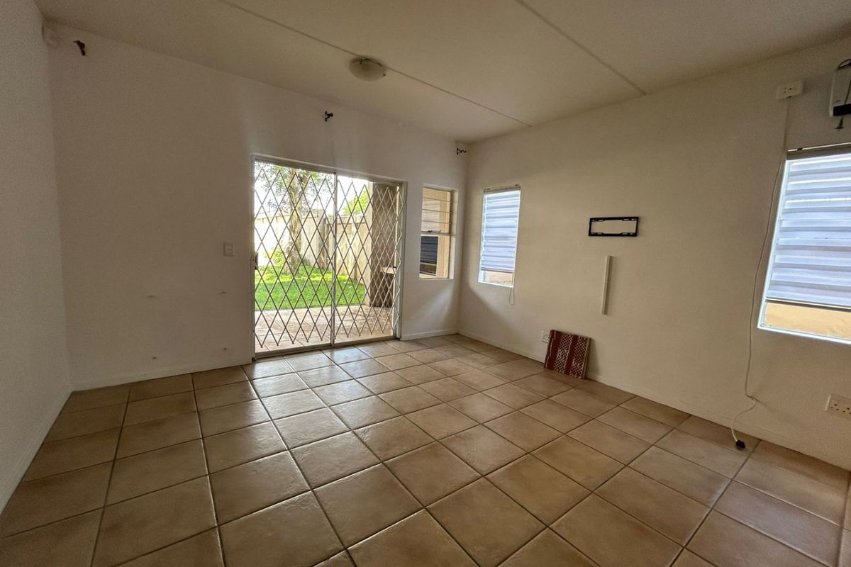 An empty living room featuring tiled flooring, sliding glass doors with security gates, and access to an outdoor patio area.