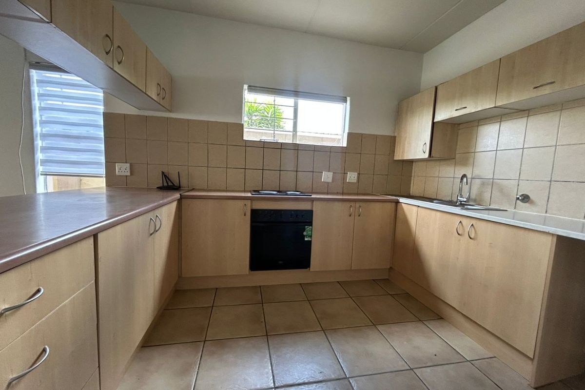 A functional kitchen featuring light wood-tone cabinetry, a built-in oven and hob, tiled flooring, and a tiled backsplash with ample counter space.