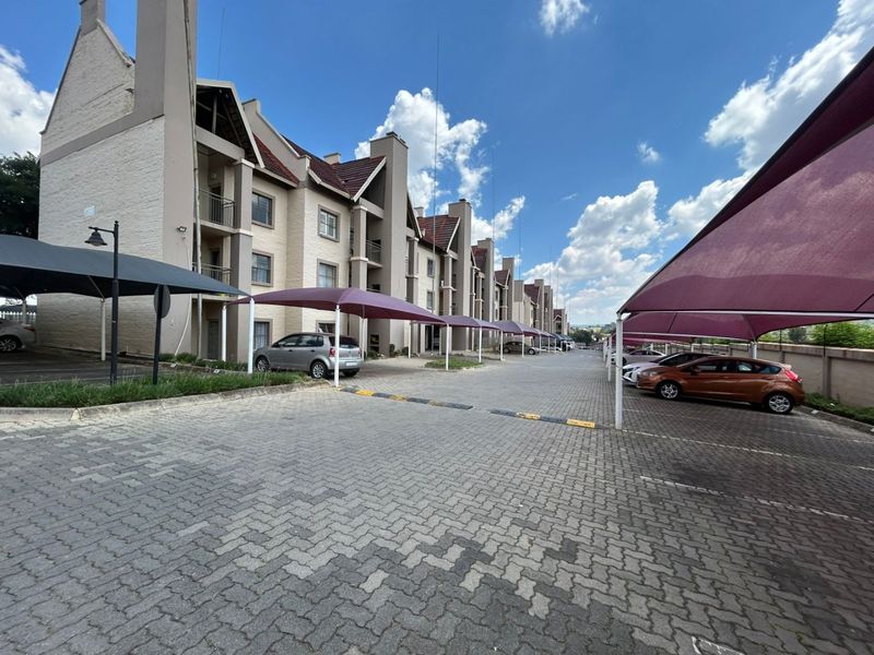 Exterior view of the apartment complex featuring paved parking areas with covered shade-cloth carports for residents.