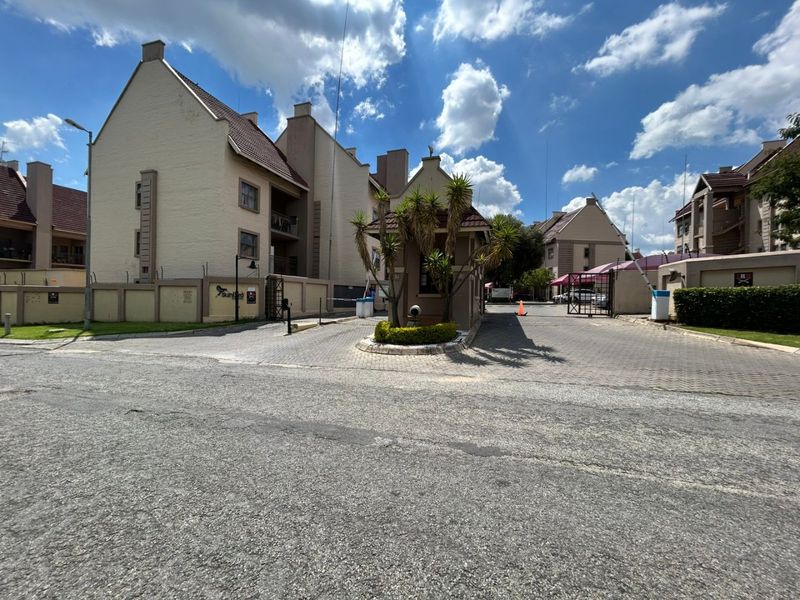 View of the apartment complex entrance featuring a security guard house, paved driveway, and perimeter walling with access control.