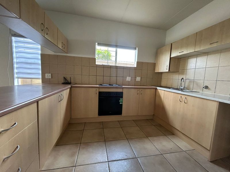 A functional kitchen featuring light wood-tone cabinetry, a built-in oven and hob, tiled flooring, and a tiled backsplash with ample counter space.