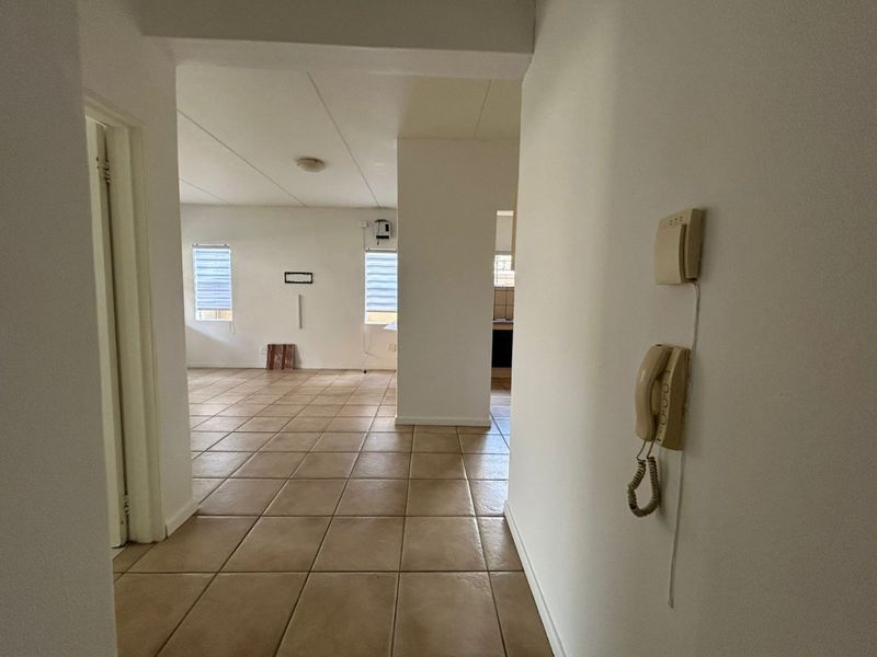 A view from the hallway looking into an open-plan living area with tiled flooring, featuring an intercom system and neutral wall finishes.
