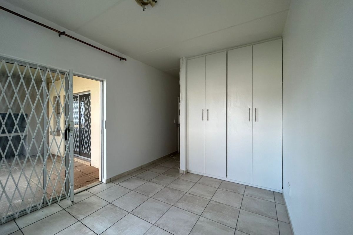 A bedroom featuring built-in white cabinetry, tiled flooring, and a security gate leading to an outdoor patio area.