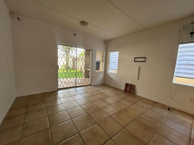 An empty living room featuring tiled flooring, sliding glass doors with security gates, and access to an outdoor patio area.