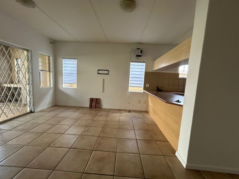 Open-plan living and kitchen area featuring tiled flooring, built-in kitchen cabinetry with a breakfast counter, and access to an outdoor patio area.