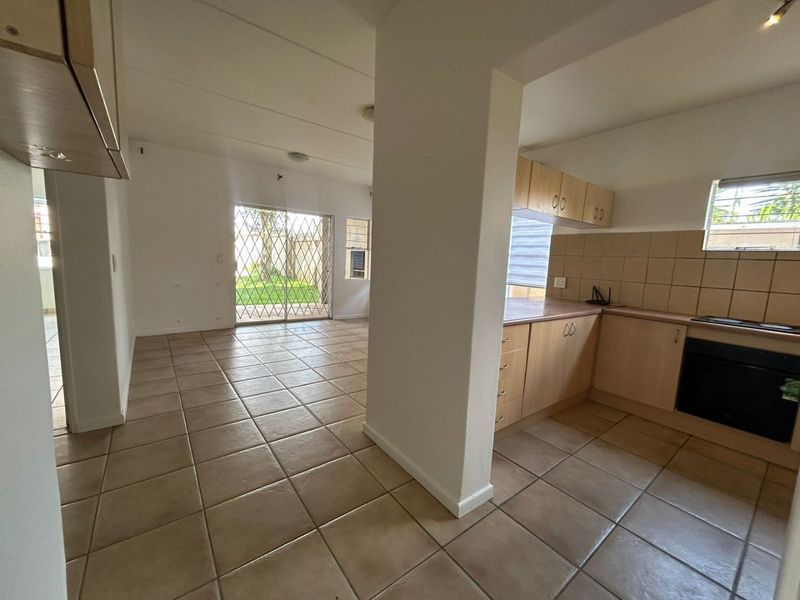 Open-plan living area featuring tiled flooring and a functional kitchen with built-in cabinetry, oven, and hob, leading to an outdoor patio space.