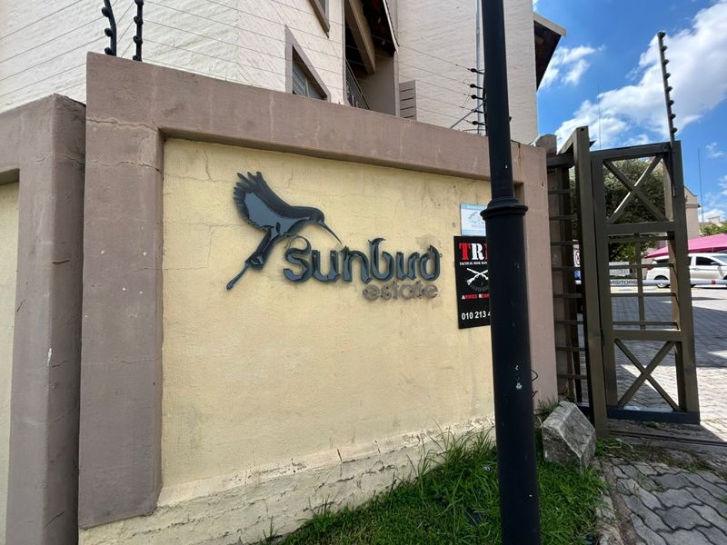 Entrance view of Sunbird Estate featuring the complex signage, security gate, and perimeter wall with electric fencing.