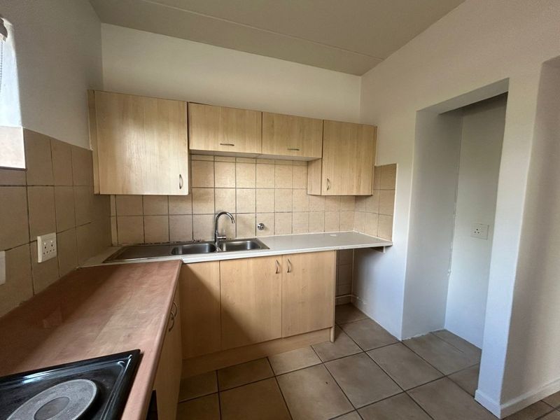 A functional kitchen featuring light wood-finish cabinetry, tiled splashbacks, a stainless steel sink, and a built-in hob.