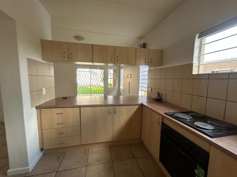 A functional kitchen featuring light wood-finish cabinetry, laminate countertops, a built-in electric hob and oven, and tiled flooring with a pass-through window.