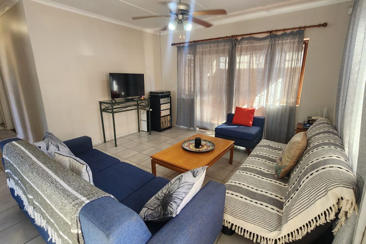 A comfortable living room featuring tiled flooring, a ceiling fan, and large windows with curtains, providing a bright and functional space.