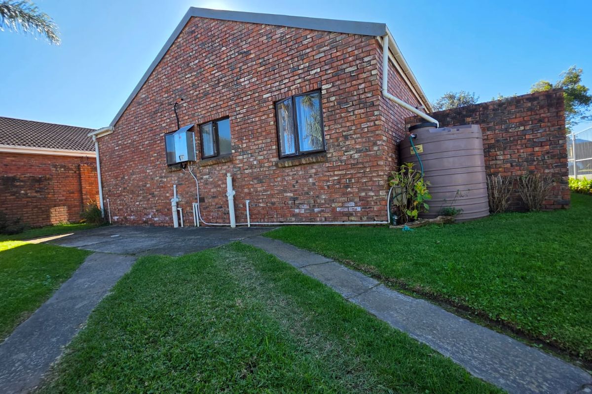 Rear view of the property featuring exposed brick facade, concrete pathways, and a large water storage tank set within a grassed garden area.