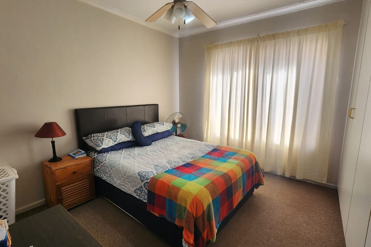 A functional bedroom featuring built-in cupboards, carpeted flooring, and a ceiling fan, offering a comfortable and practical living space.