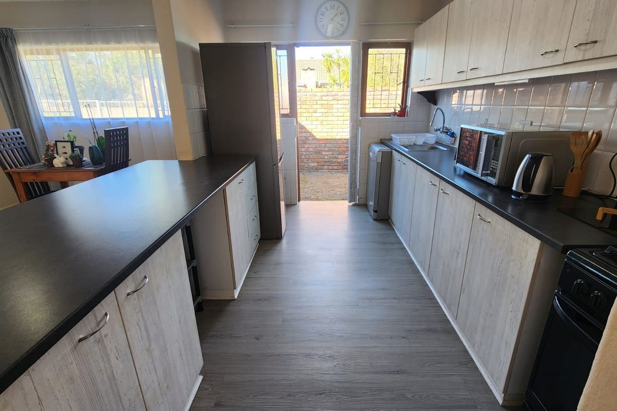 A functional kitchen featuring light wood-grain cabinetry, dark countertops, and a breakfast bar, with direct access to an outdoor area.