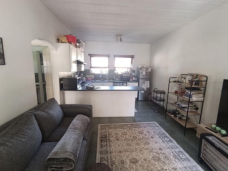 Open-plan living area featuring a functional kitchen with a breakfast bar, tiled flooring, and direct access to an adjacent room.