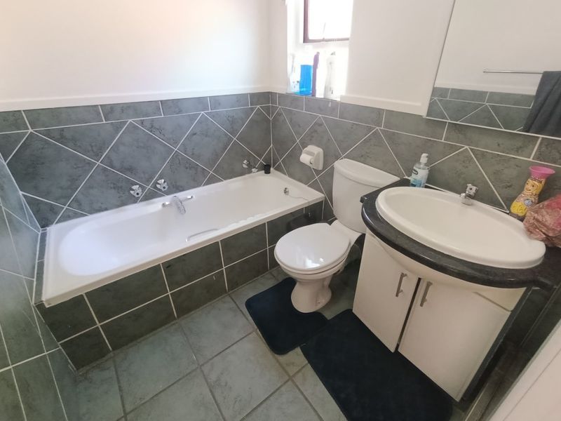 A functional bathroom featuring a built-in bathtub, a vanity unit with a basin, and a toilet, finished with grey tiled walls and flooring.