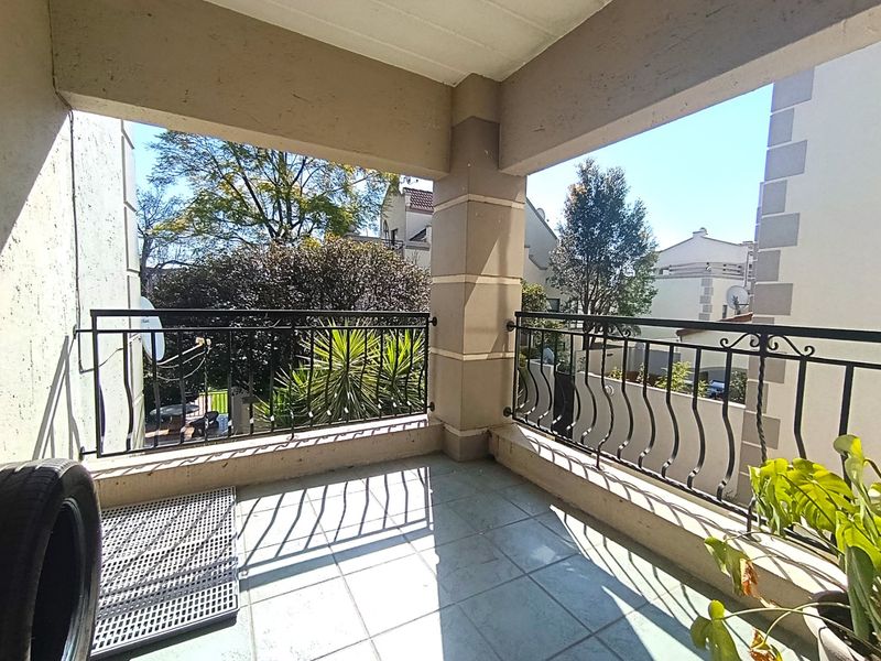 A covered balcony featuring tiled flooring and decorative wrought iron railings, offering an open view of the surrounding residential complex.