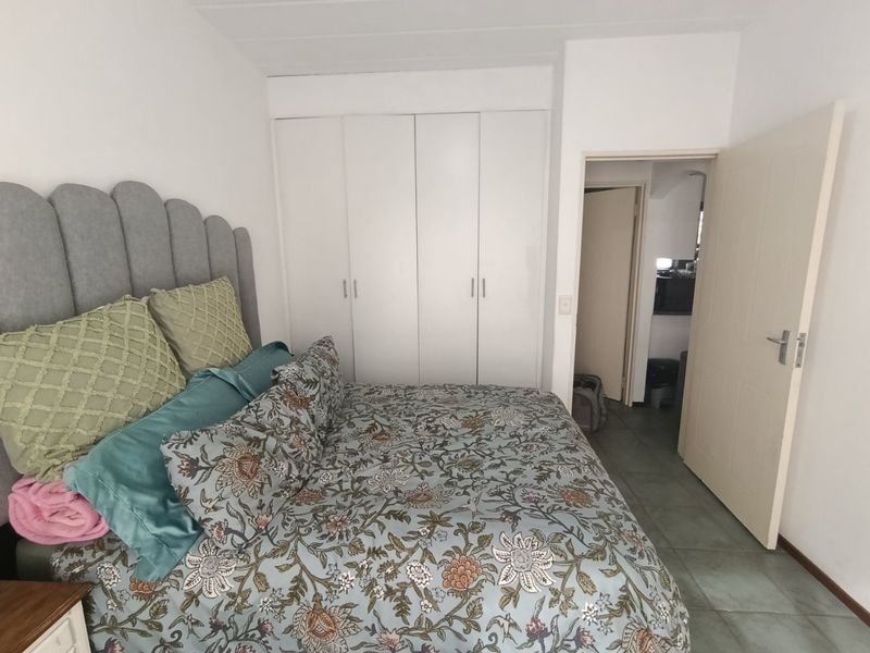 A bedroom featuring built-in cupboards and tiled flooring, with an adjacent doorway leading to a secondary room.