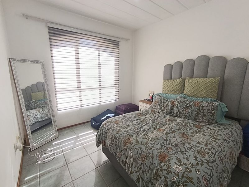 A bedroom featuring tiled flooring, a large window with fitted blinds, and a neutral wall finish.