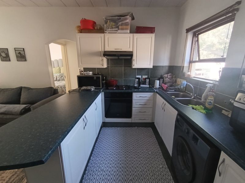 Compact kitchen featuring white cabinetry, dark laminate countertops, integrated oven, extractor fan, and a double basin sink with adjacent laundry plumbing.