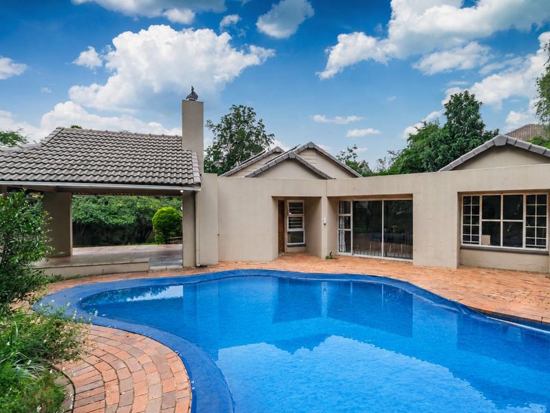 Rear exterior view featuring a swimming pool, brick paved patio area, and a covered outdoor entertainment space with a built-in chimney.