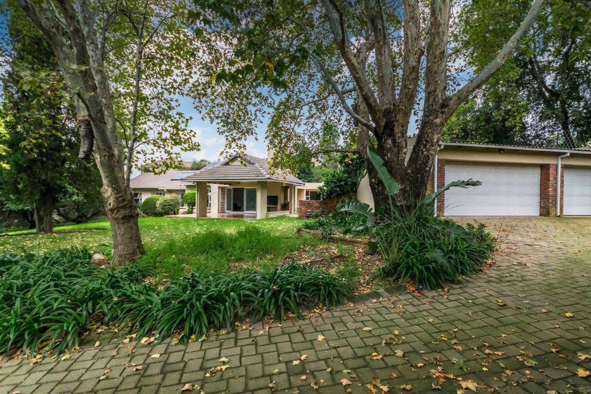 A view of the rear garden featuring a covered patio, mature trees, and a double garage with paved driveway access.