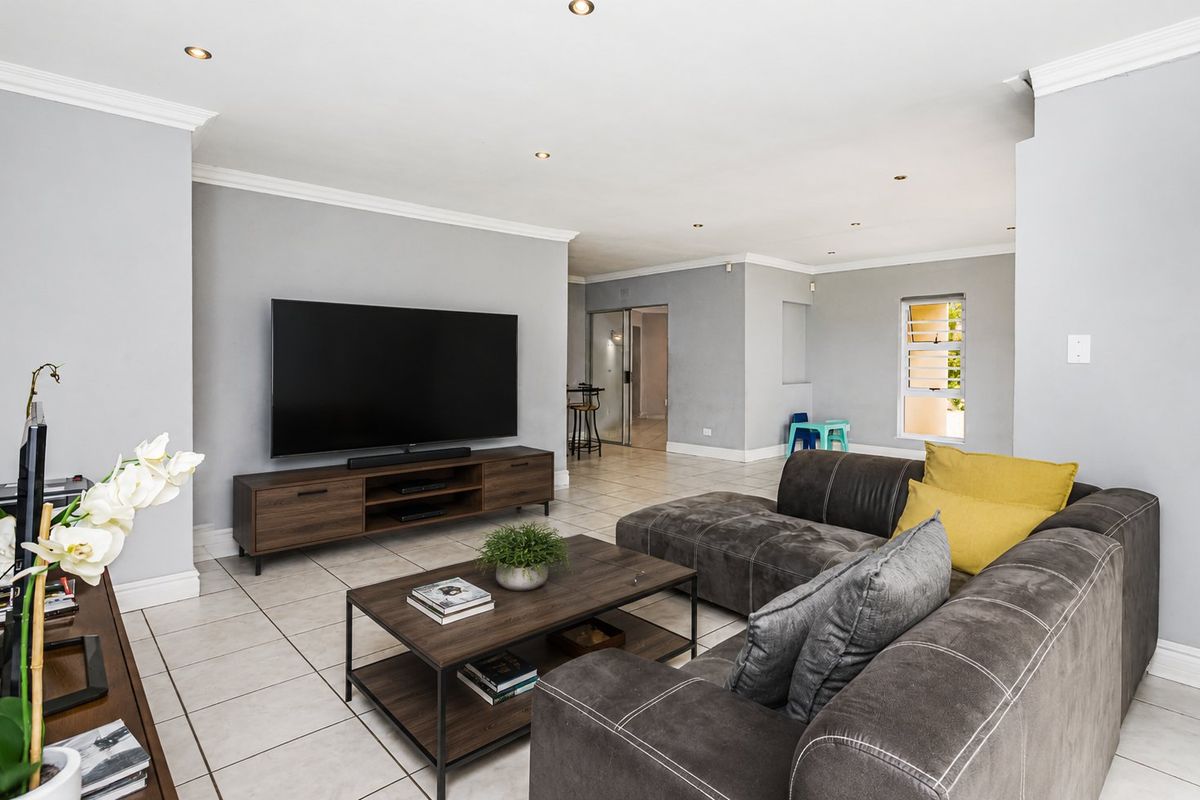 Spacious open-plan living area featuring neutral grey walls, tiled flooring, recessed downlighting, and crown molding throughout.