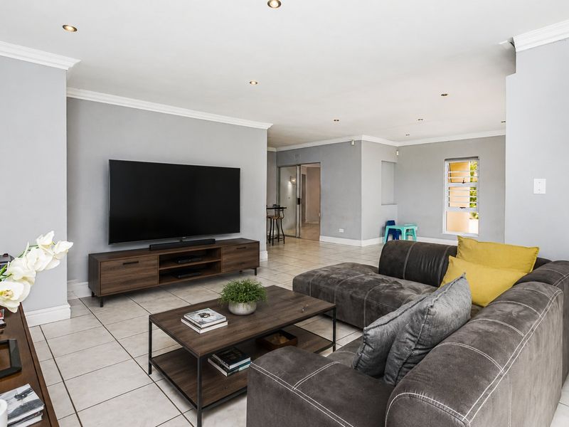 Spacious open-plan living area featuring neutral grey walls, tiled flooring, recessed downlighting, and crown molding throughout.